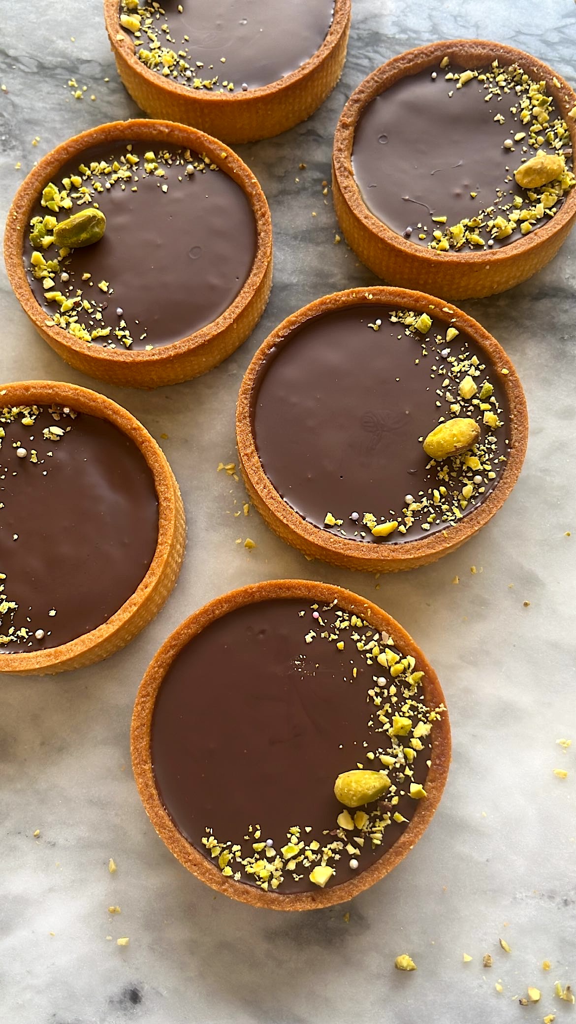 A chocolate tart topped with sliced pistachios arranged decoratively